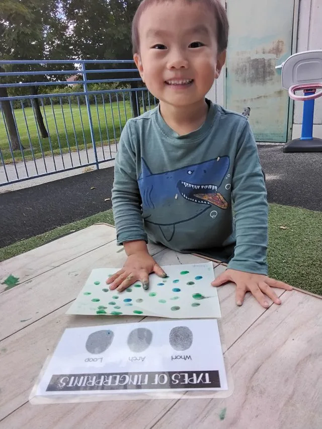 Toddler standing outside doing finger painting.
