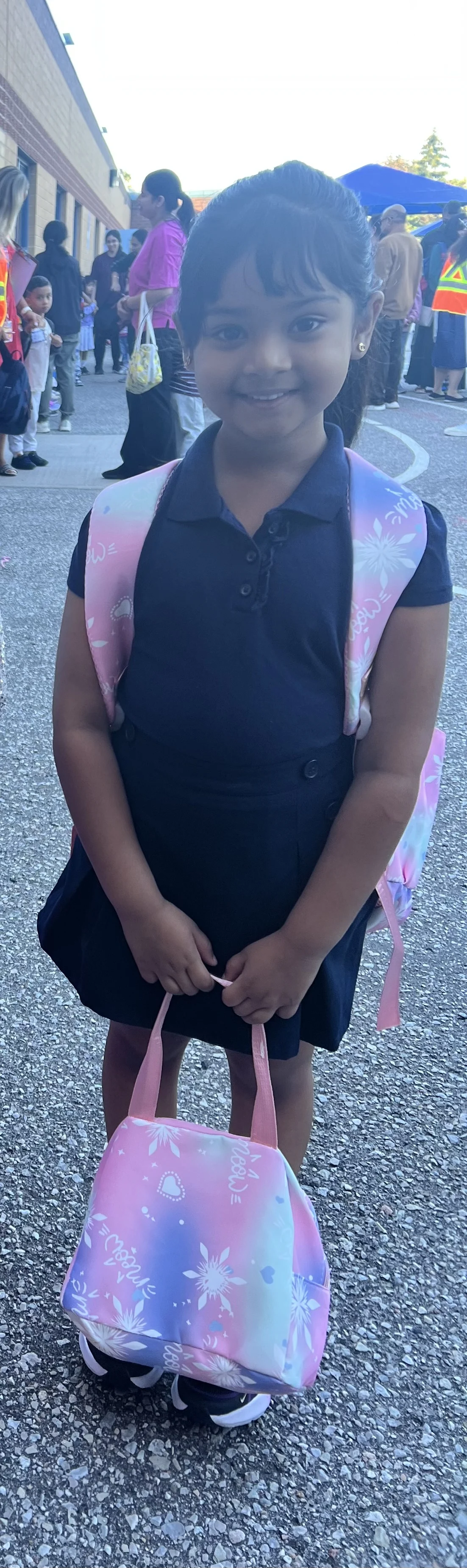 A young child in a blue top and pink backpack smiles.