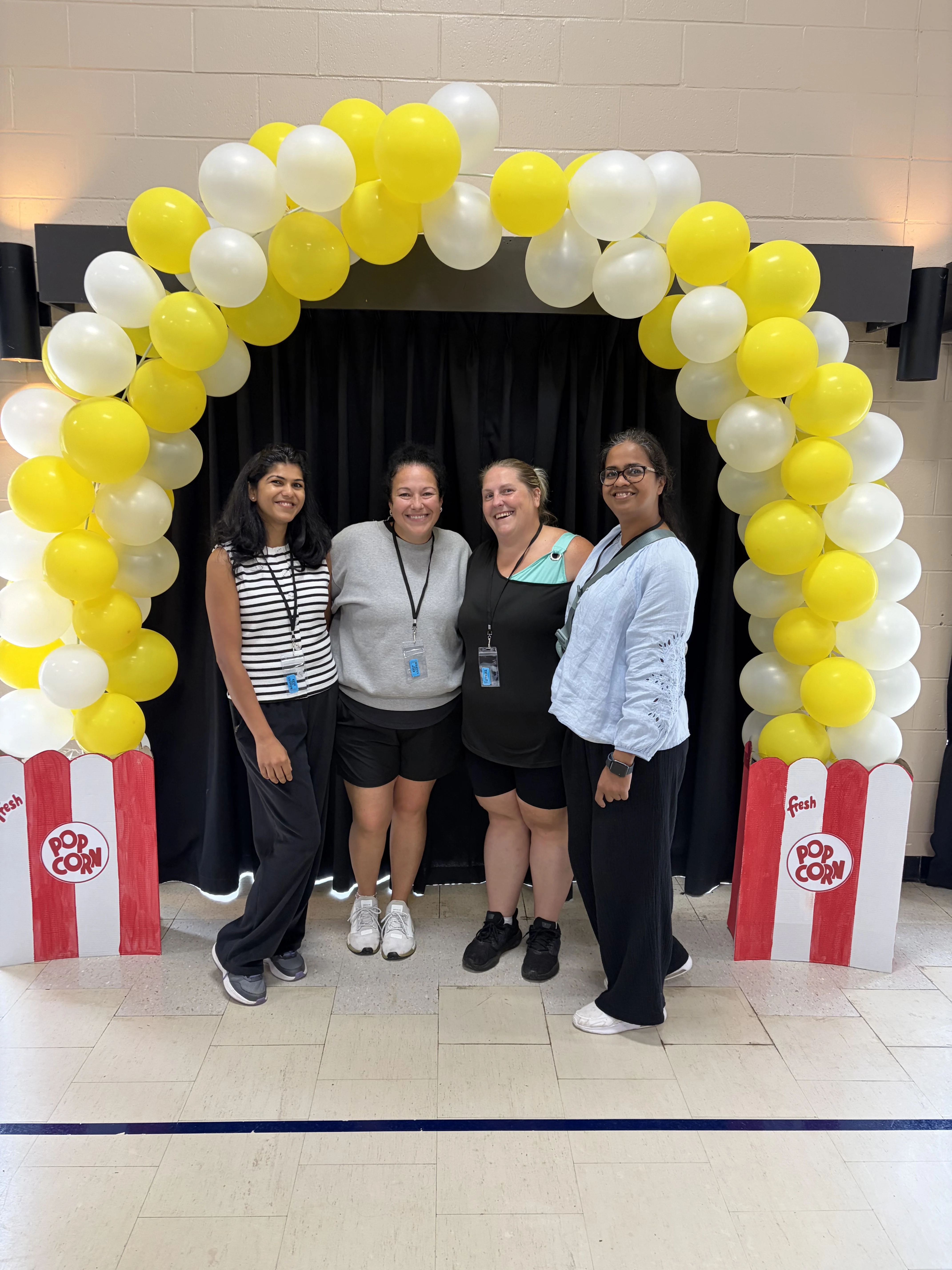 Four adults stand under a balloon arch