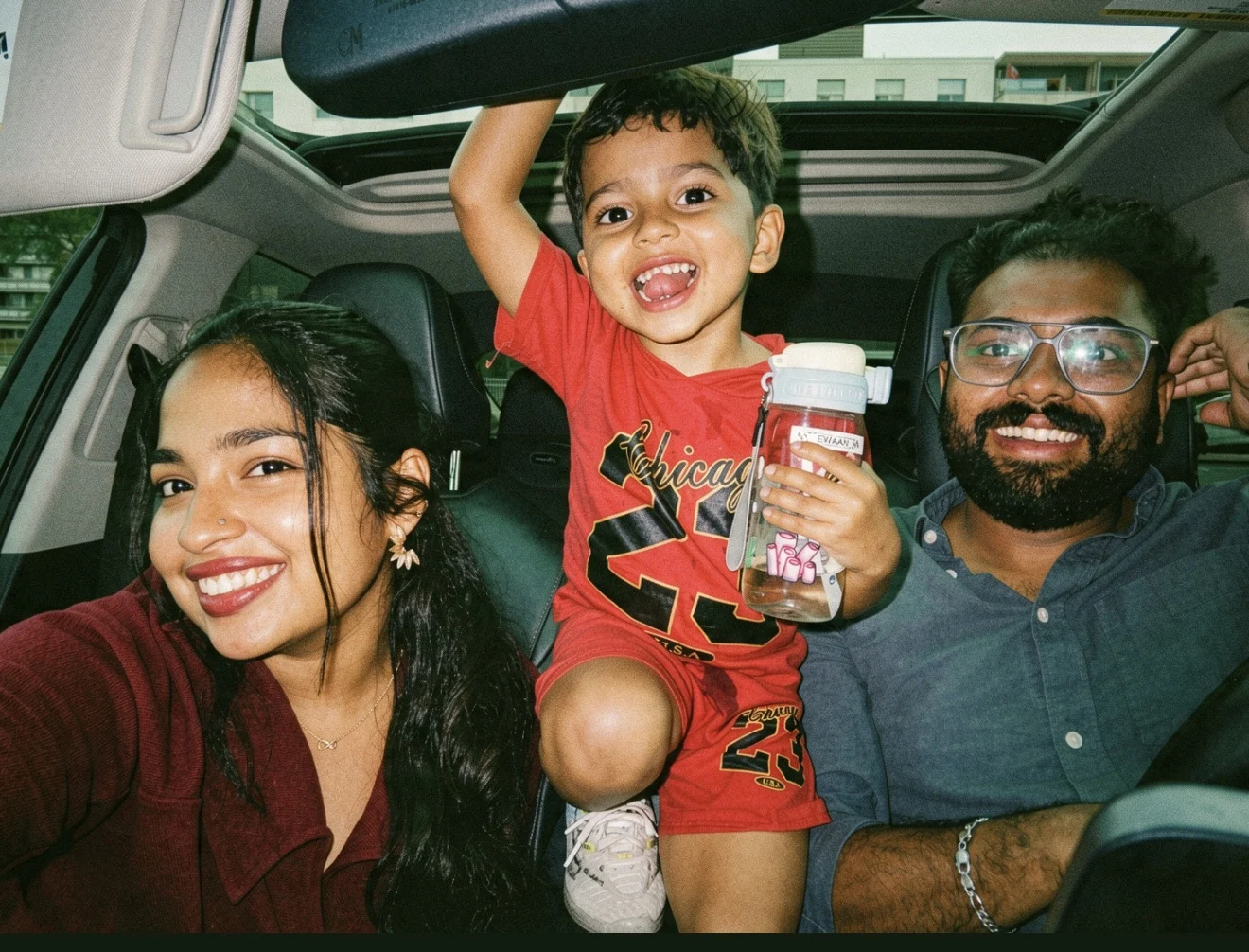 Two adults with kid inside a vehicle, smiling.