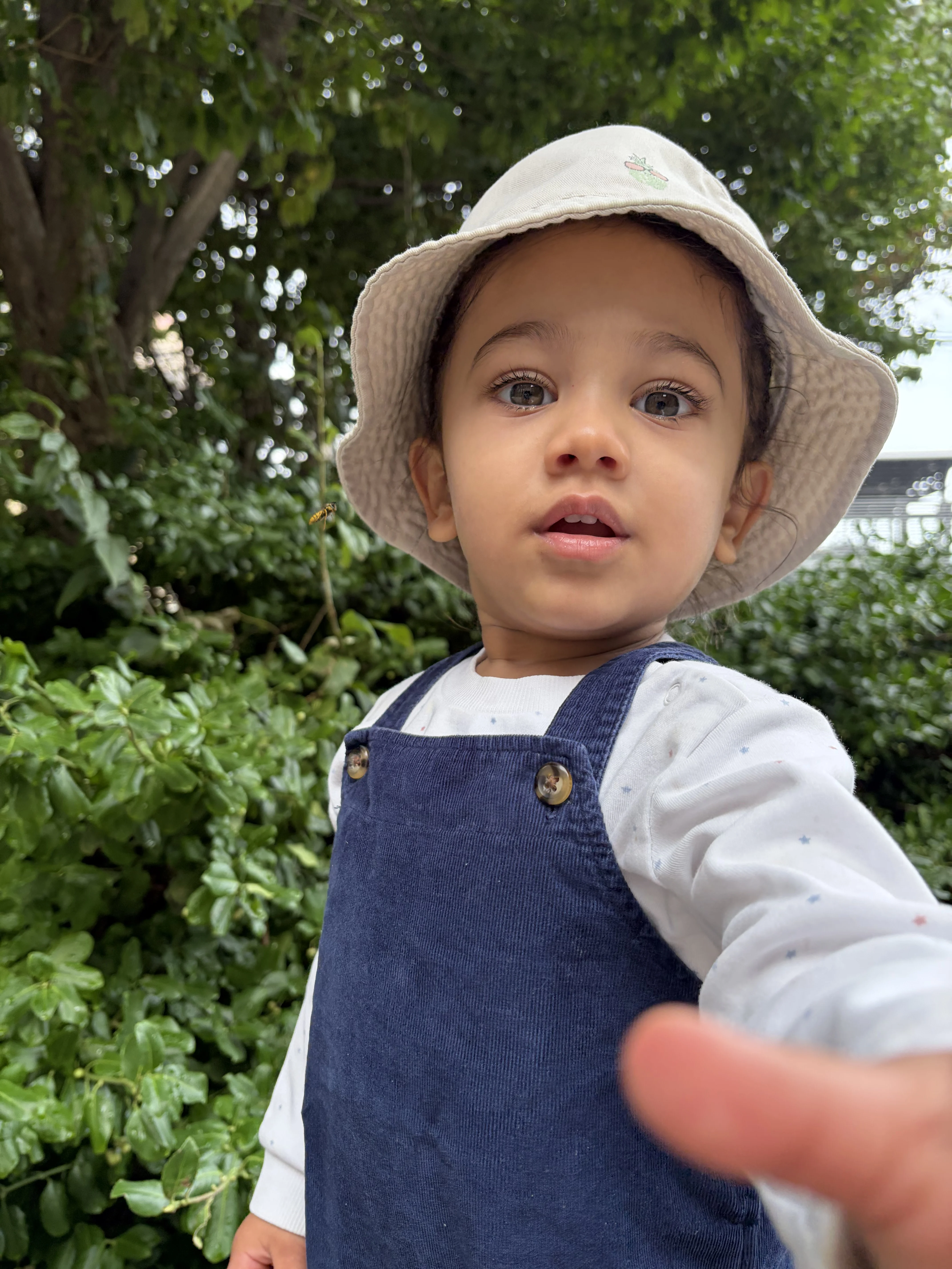 Young child outside with a bucket hat and overalls on.