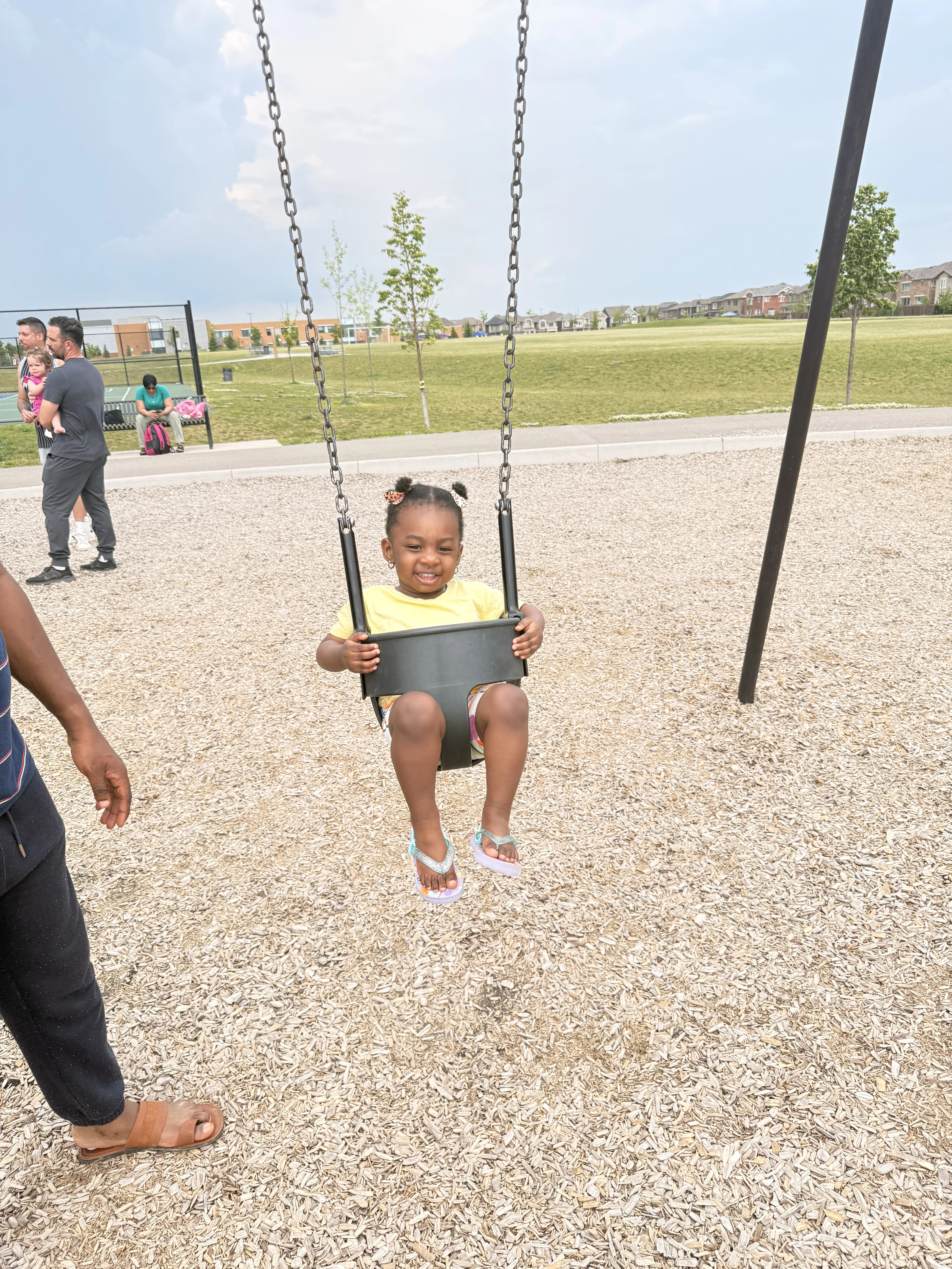 A smiling child in a yellow t-shirt sits on a swing in a playground.