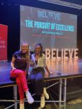 Sarah Wells and Tyra Daniels sit on a stage, smiling.