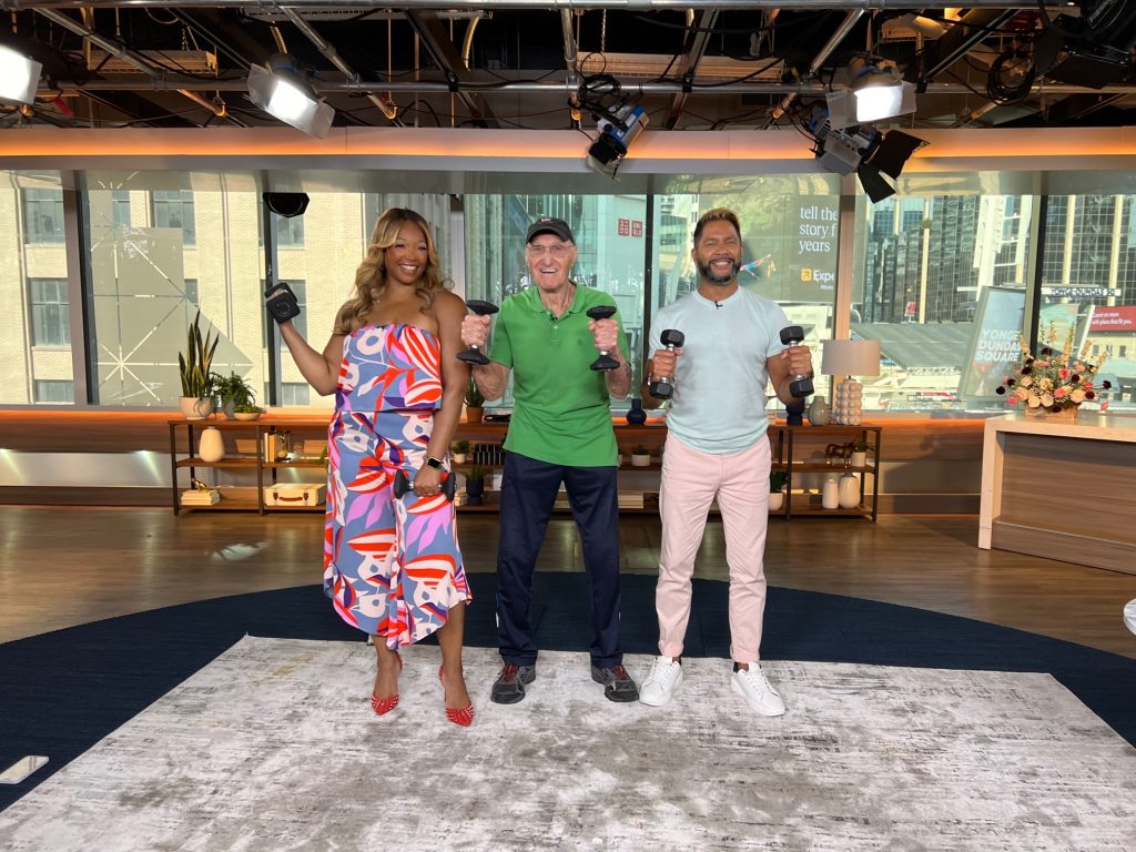 Vic Downs stands between two hosts in the Breakfast Television studio.