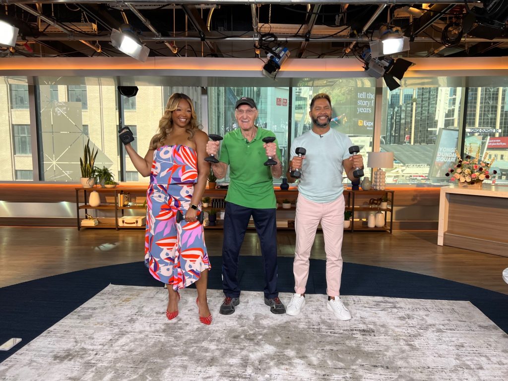 Vic Downs stands between two hosts in the Breakfast Television studio.