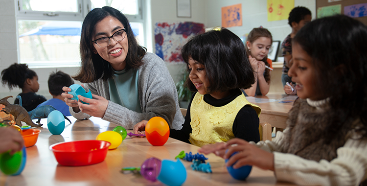 An educator holds a split plastic blue toy egg to teach two children about dinosaurs and dinosaur eggs.